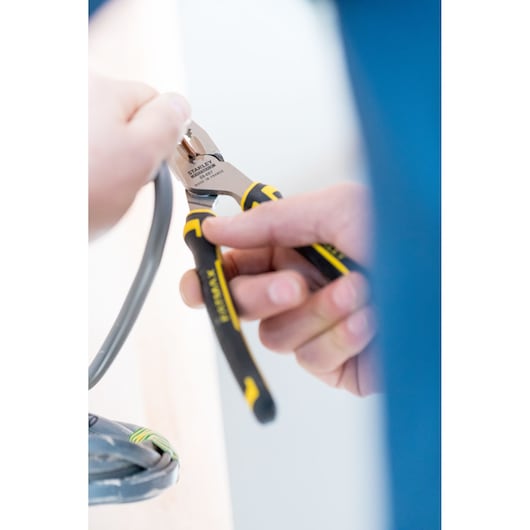 STANLEY 0-89-867 diagonale kniptang met zwart-gele handgrepen knipt een grijze kabel, close-up.