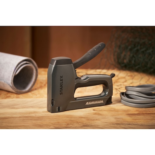 Agrafeuse en aluminium STANLEY 0-TR250 sur une surface en bois, vue latérale, matériaux roulés à côté.