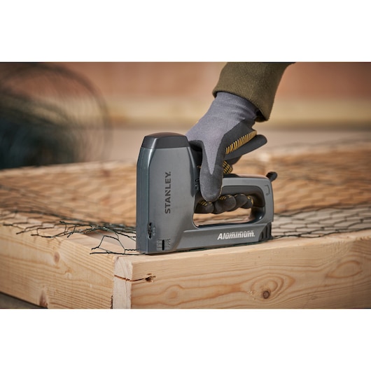 Stanley 0-TR250 agrafeuse en aluminium utilisée pour fixer un grillage sur un cadre en bois, vue latérale.