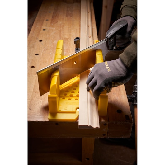 STANLEY 1-20-600 photographie d'une boîte à onglets jaune et d'une scie coupant une moulure en bois sur établi, vue en angle.