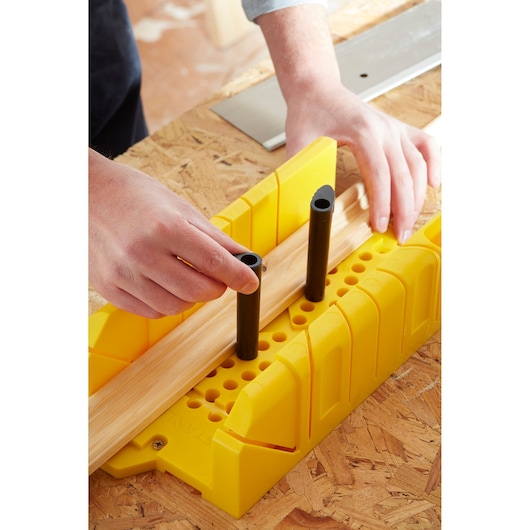 STANLEY 1-20-600 gele verstekbak op werkbank, met hout en handen die zwarte pinnen plaatsen.