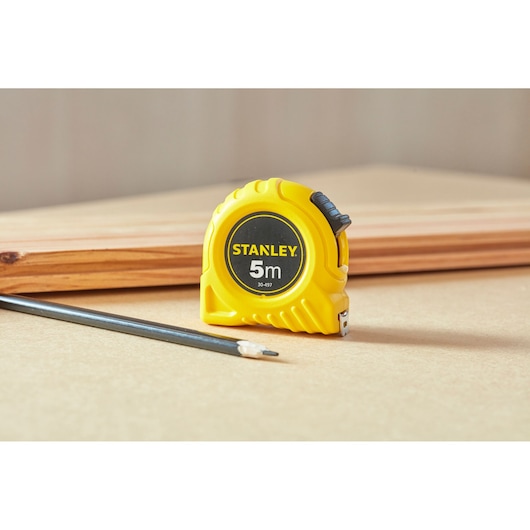 Stanley 1-30-497 rolmaat in gele behuizing, naast potlood en hout, productfotografie.