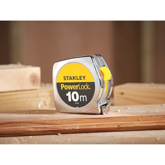 STANLEY 1-33-442 PowerLock mètre ruban 10m avec bouton jaune sur surface en bois, vue latérale.