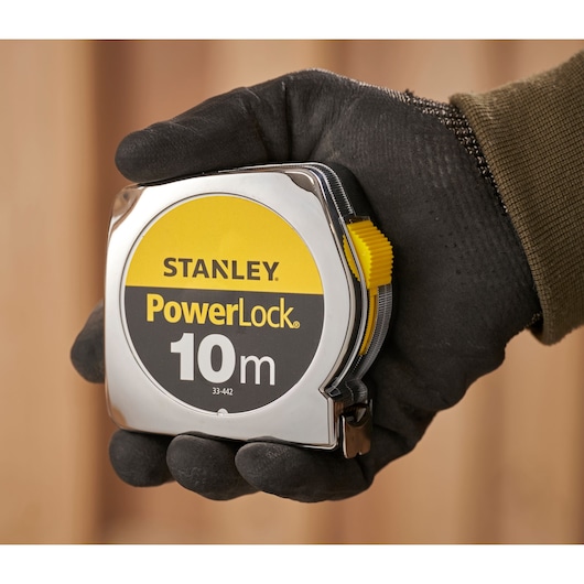 STANLEY 1-33-442 PowerLock mètre ruban 10m tenu dans une main gantée, photographie en gros plan.