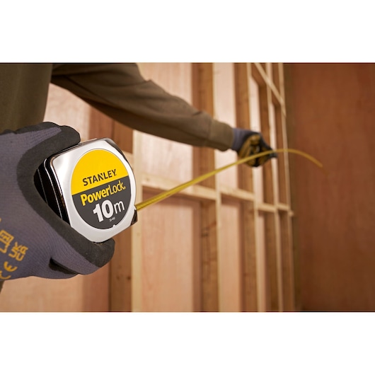 Personne utilisant le mètre ruban STANLEY 1-33-442 PowerLock 10m pour mesurer une charpente en bois.