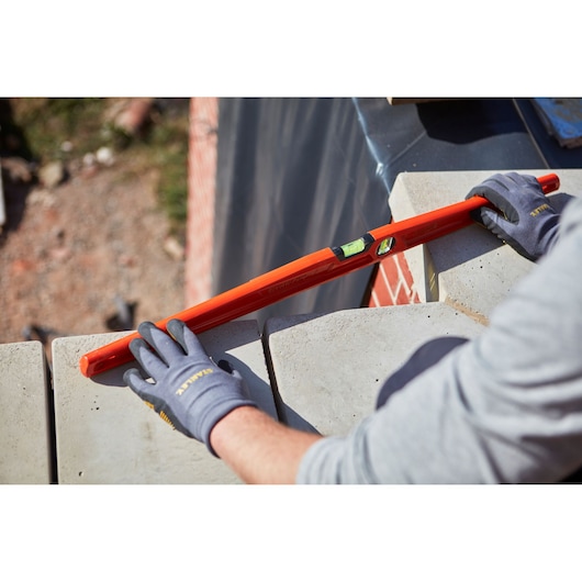 STANLEY 1-42-315 waterpas gebruikt op metselwerk door gehandschoende handen, productfotografie, hoekaanzicht.