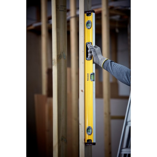 STANLEY 1-43-536 waterpas verticaal tegen houten balk gehouden, gehandschoende hand toont gebruik op bouwplaats.
