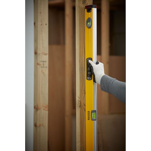STANLEY 1-43-548 waterpas verticaal tegen houten frame gehouden, gebruiker draagt handschoen.