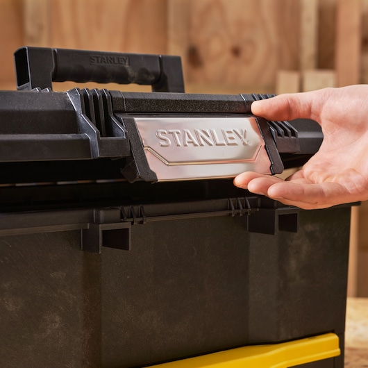 STANLEY 1-70-316 gereedschapskist close-up in zwart en geel, hand opent de sluiting.