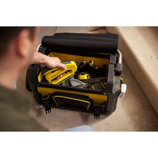 Photo du sac à outils STANLEY 1-79-213 avec dessus ouvert, contenant des outils jaunes et noirs sur le sol.