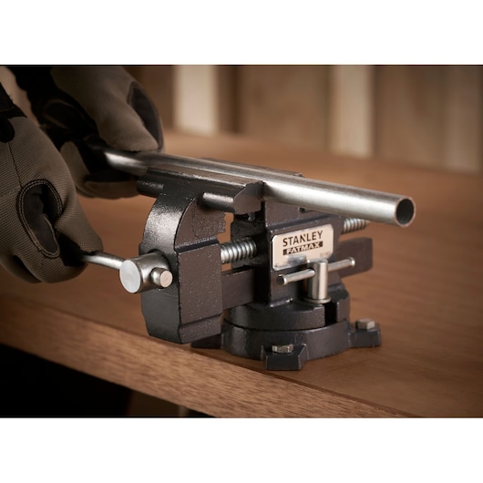 STANLEY 1-83-065 bankschroef klemt metalen buis op houten werkbank, close-up zijaanzicht.