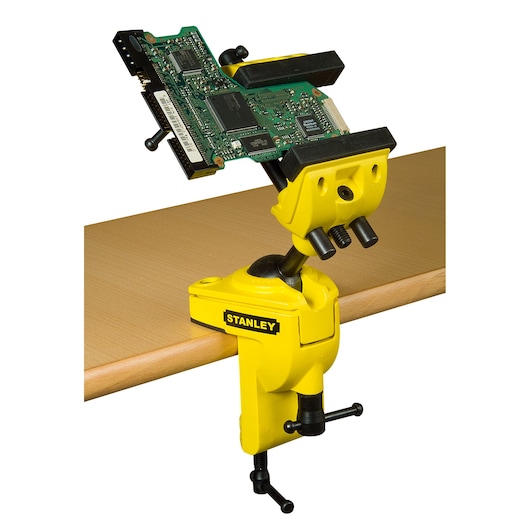 STANLEY 1-83-069 bankschroef met gele behuizing en verstelbare bek, bevestigd aan tafel met printplaat, zijaanzicht.