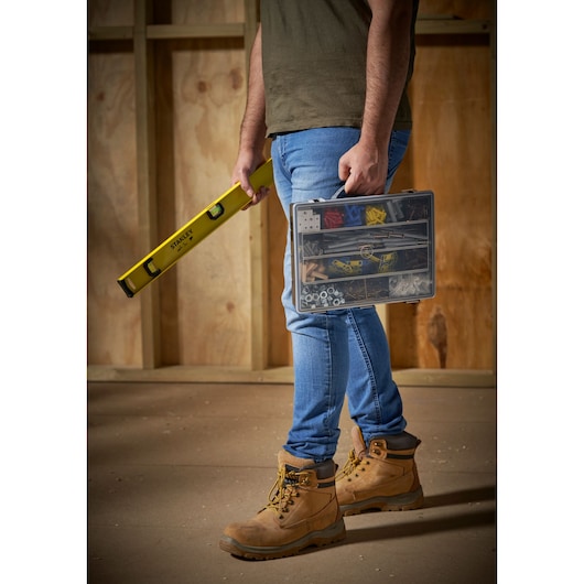 STANLEY 1-92-761 hardware organiser koffer, vastgehouden door persoon met beige werkschoenen op bouwplaats.