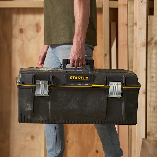 Foto van STANLEY 1-93-935 zwarte gereedschapskist met gele accenten, gedragen aan handvat, vooraanzicht.