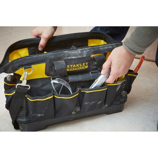 Sac à outils STANLEY 1-93-950 jaune et noir, ouvert avec une main, outils et lunettes de protection visibles.