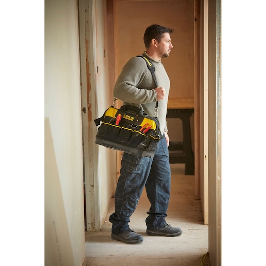 Ouvrier portant le sac à outils STANLEY 1-93-950 avec bandoulière, rempli d’outils à main, sur un chantier intérieur.