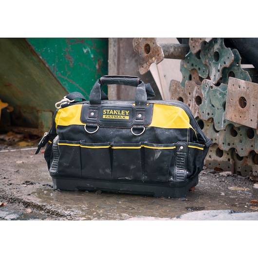 Sac à outils STANLEY 1-93-950 en tissu jaune et noir, plusieurs poches, poignées, posé dehors sur sol mouillé.