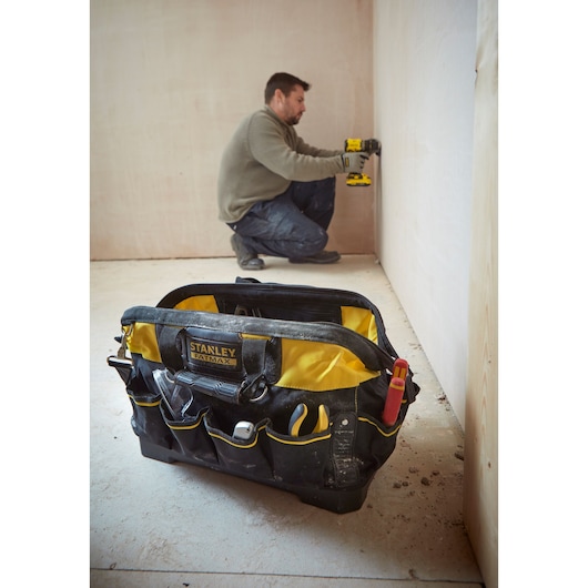 Photographie du sac à outils STANLEY 1-93-950 avec outils, avant-plan sur chantier, ouvrier en arrière-plan.
