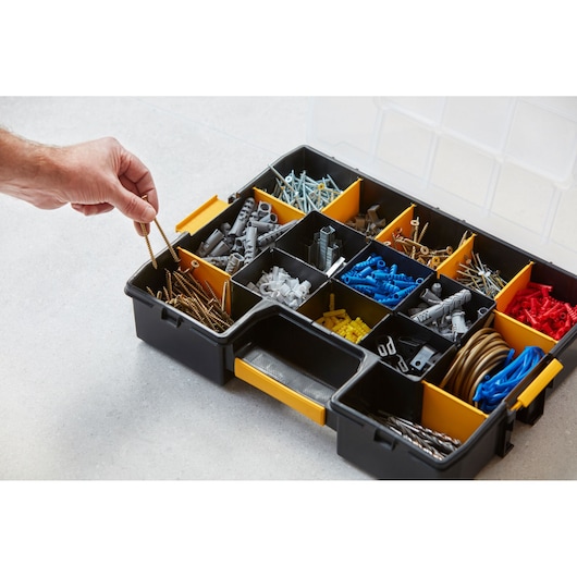 Boîte de rangement STANLEY 1-94-745 avec compartiments pour vis, chevilles et accessoires, personne prenant des vis.