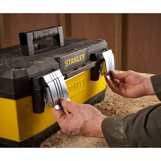 Stanley 1-95-612 boîte à outils avec loquets métalliques, mains ouvrant vue de face, design jaune et noir.