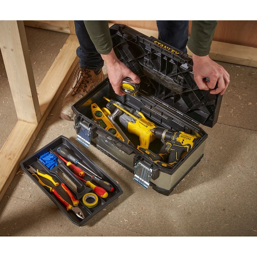Boîte à outils STANLEY 1-95-618 avec couvercle ouvert, contenant perceuses, mètre ruban, niveau et outils à main au sol.