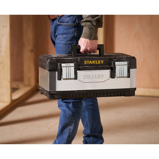 STANLEY 1-95-618 boîte à outils avec attaches métalliques, noir et argent, portée par une personne en jean.