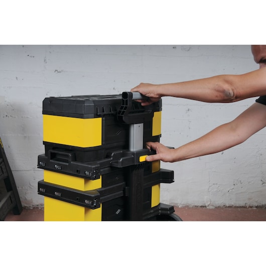 STANLEY 1-95-621 boîte à outils empilable sur chariot, jaune et noire, manipulée par une personne dans un atelier.