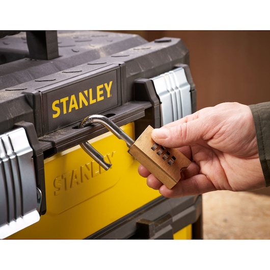 STANLEY 1-95-829 gereedschapskist geel met zwart, close-up, met open combinatieslot vastgehouden door een hand.