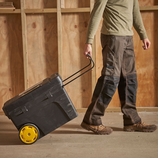 STANLEY 1-97-503 boîte à outils à roulettes avec roues jaunes tirée par une personne dans un atelier intérieur.