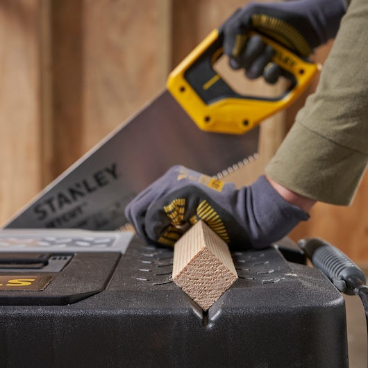 STANLEY 1-97-503 scie coupe du bois sur une boîte à outils noire, gros plan, travailleur avec des gants.