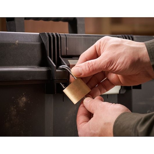 Close-up van handen die een zwarte gereedschapskist vergrendelen met een messing hangslot.