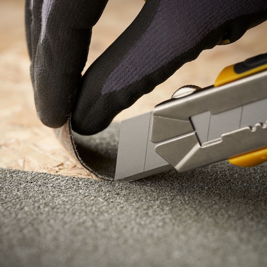 STANLEY 2-11-725 stanleymes snijdt dakmateriaal, close-up, gehandschoende hand houdt materiaal vast.