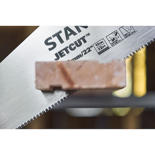 Scie à main STANLEY 2-15-244 coupant du bois en gros plan, montrant les dents JetCut et les détails du produit.