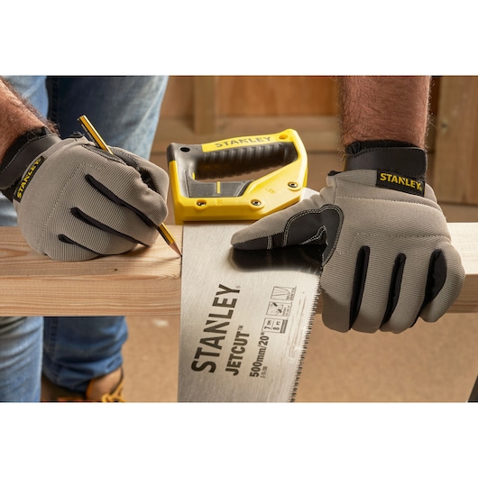 Photographie de STANLEY 2-15-288 scie à main et gants marquant du bois, poignée jaune visible en atelier.