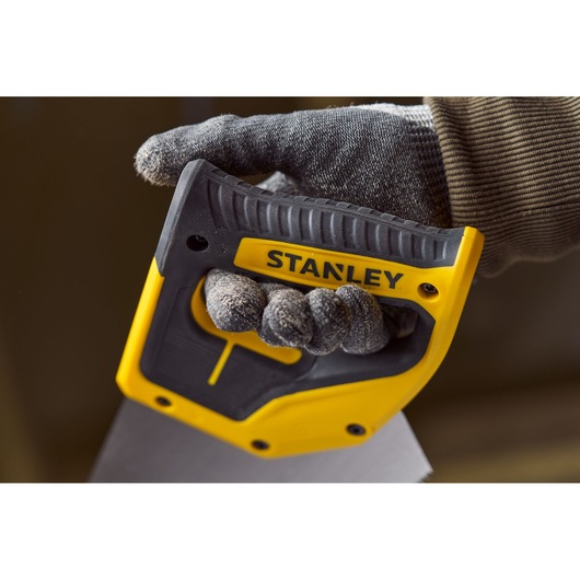 Photo d'une main gantée tenant la poignée ergonomique jaune et noire de la scie STANLEY 2-20-037 en gros plan.