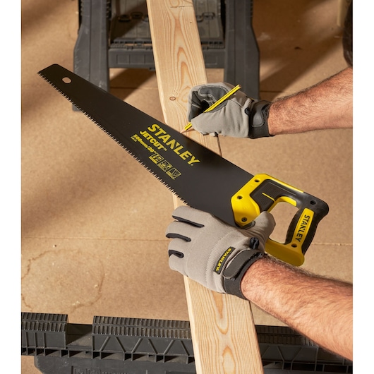 STANLEY 2-20-151 handzaag met geel-zwart handvat zaagt een houten plank, werker draagt handschoenen.