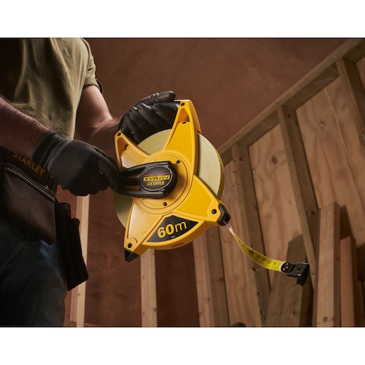 Stanley 2-34-824 gele 60m meetlint vastgehouden door een gehandschoende hand op bouwplaats.