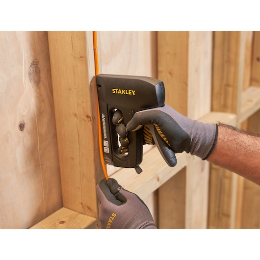 Stanley 6-CT-10X agrafeuse fixant un câble orange sur une structure en bois, vue rapprochée.