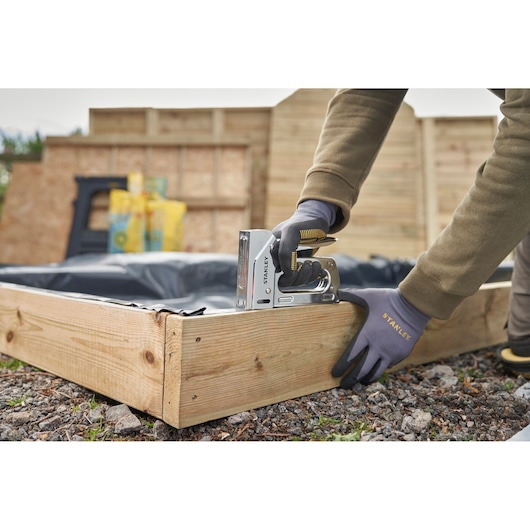 Foto van de STANLEY 6-TR110 tacker die een plastic folie aan een houten plantenbak buiten vastzet.
