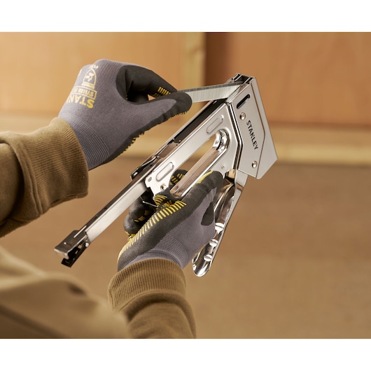 Stanley 6-TR110 nietmachine vastgehouden door handschoenen, nietjes plaatsen, close-up.
