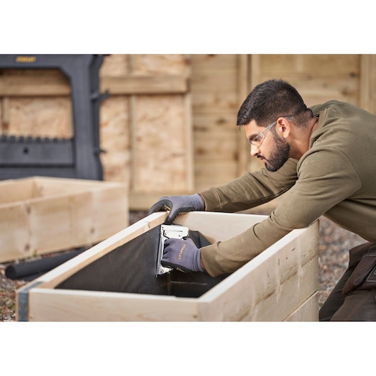Agrafeuse STANLEY 6-TR45 utilisée par une personne avec des gants pour assembler un bac en bois, en extérieur.