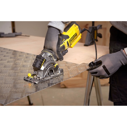 STANLEY FME380K scie circulaire compacte découpant une tôle métallique, gros plan sur mains gantées, atelier.