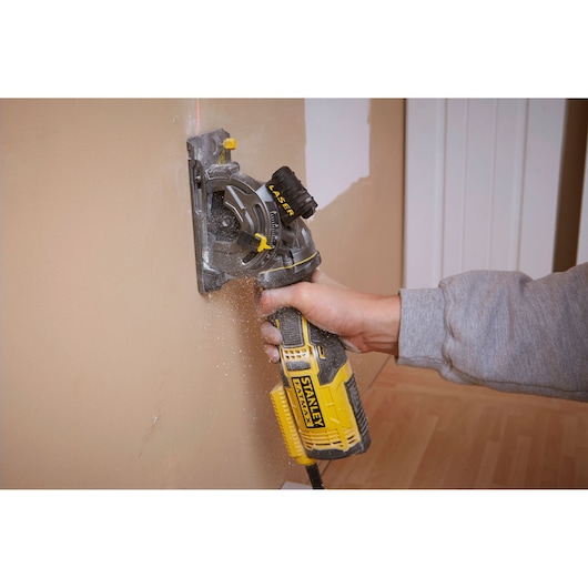 Photo de la rainureuse STANLEY FME380K en utilisation, découpant un mur en plâtre.
