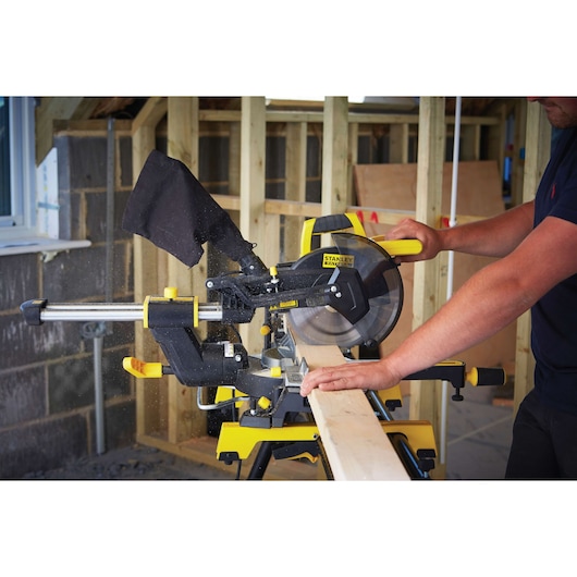 STANLEY FME721 verstekzaag zaagt hout in werkplaats, zijaanzicht met stofzak en gele details.