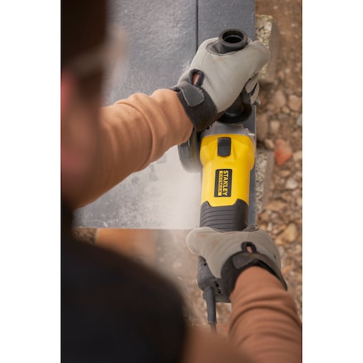 Foto van STANLEY FMEG225VS haakse slijper gebruikt op steen door handschoenen buiten.