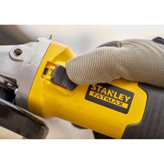 STANLEY FMEG225VS haakse slijper close-up, gehandschoende hand op schakelaar, geel en zwart lichaam.