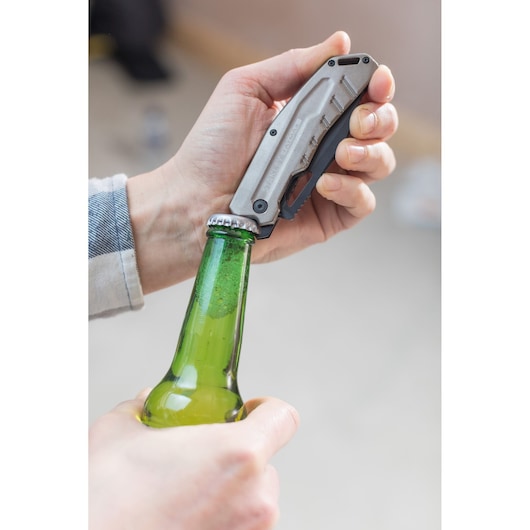Photo du couteau utilitaire pliant STANLEY FMHT0-10312 utilisé pour ouvrir une bouteille en verre verte.