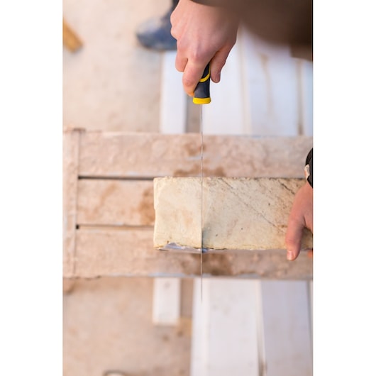 STANLEY FMHT0-10327 scie à main coupant une brique beige, vue de dessus, environnement de chantier.