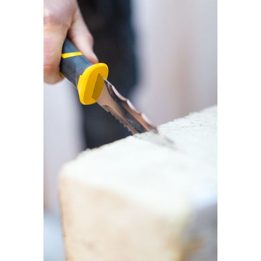 Couteau STANLEY FMHT0-10327 à lame dentelée et manche noir et jaune découpant un matériau clair, gros plan.