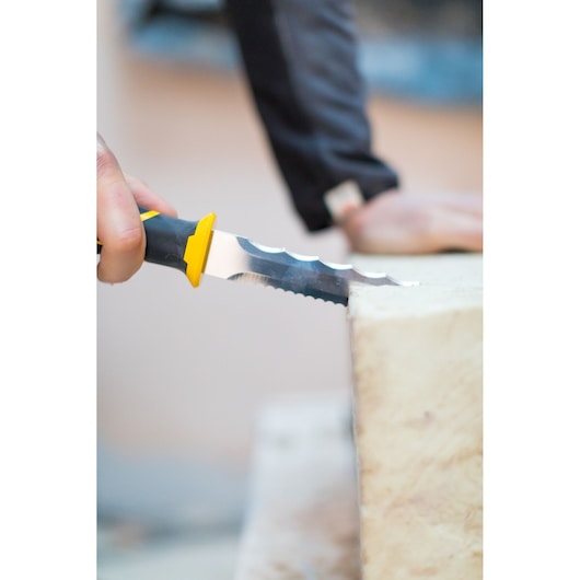 Photographie du couteau d’isolation STANLEY FMHT0-10327 à lame dentelée coupant un matériau isolant jaune.